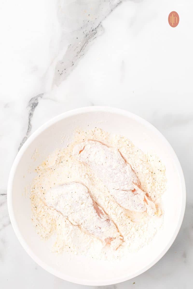 2 pieces of chicken on a bowl of flour mixture.