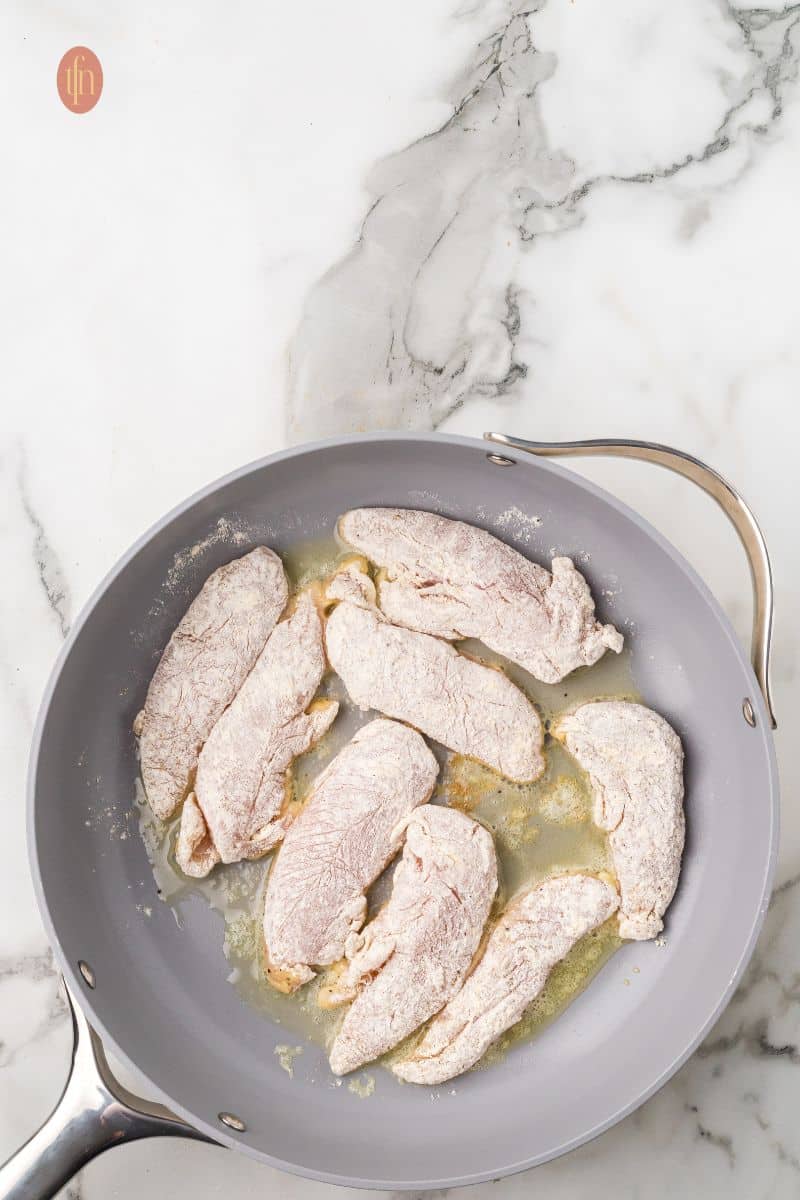 Flour covered chicken on a frying pan.