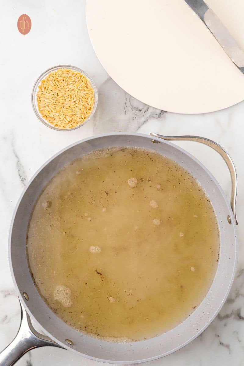 A pan of liquid mixture with a bowl of orzo.