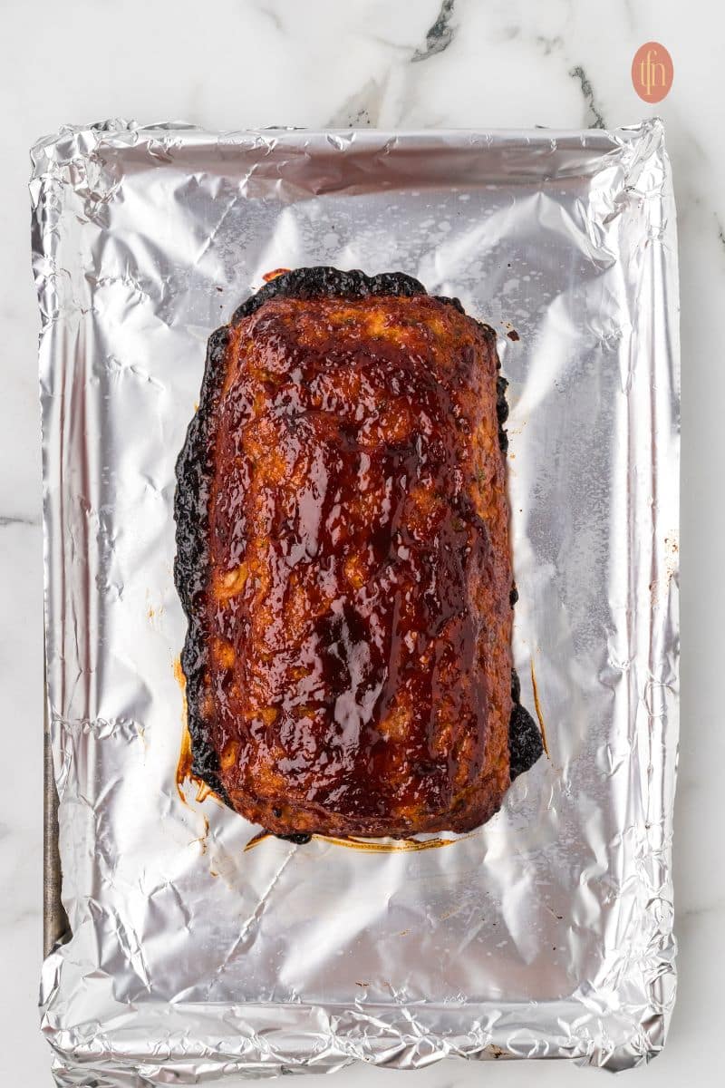 An overhead shot of the fully baked chicken meatloaf on the foil-lined baking sheet, covered in a glossy, dark red glaze.