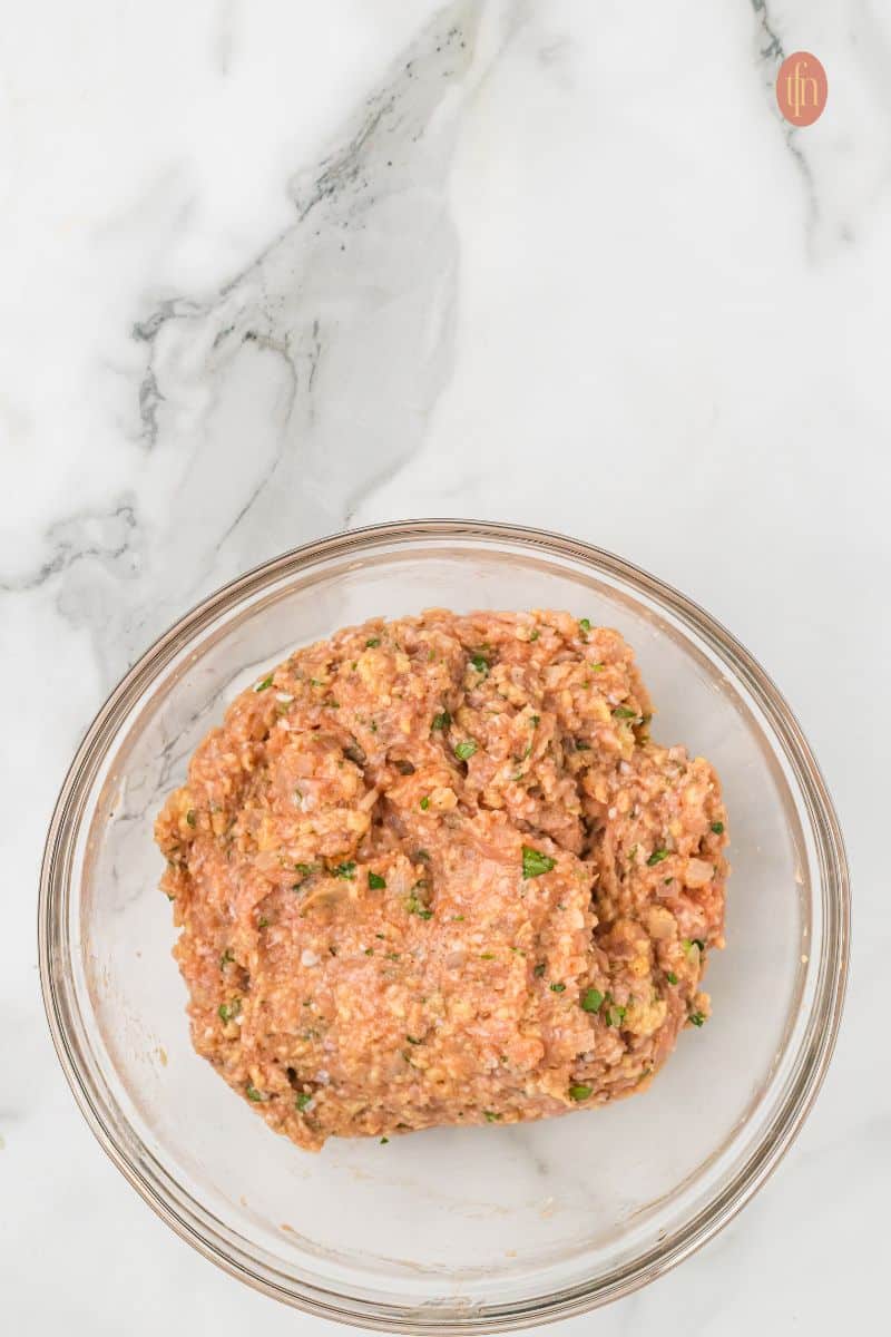 A large glass bowl holds the finished raw chicken meatloaf mixture, which is uniformly combined and ready to be shaped.