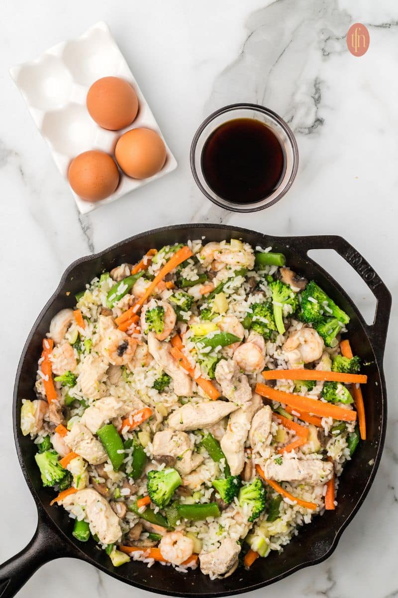 A skillet pan of fried rice., A tray of eggs and a bowl of black liquid.
