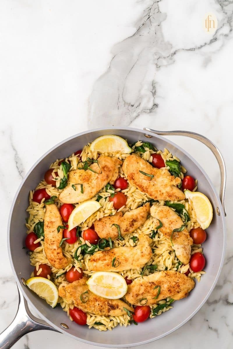 A pan of chicken and orzo with garnish.