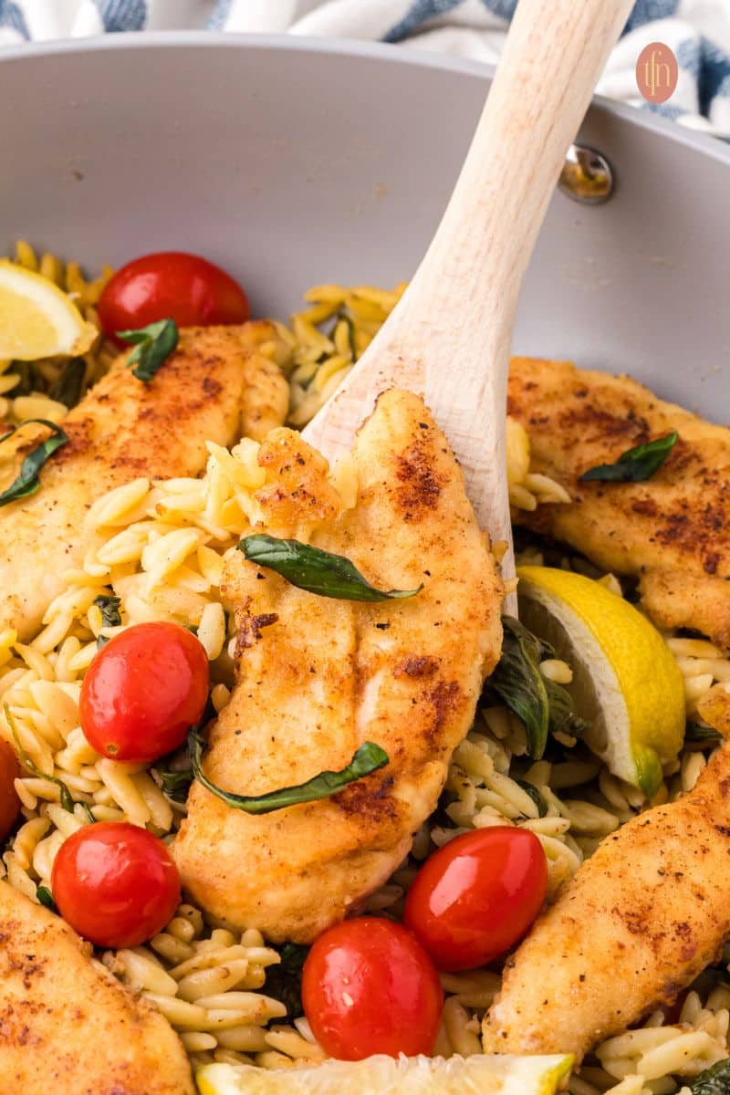 A scoop of chicken on a pan of orzo chicken.