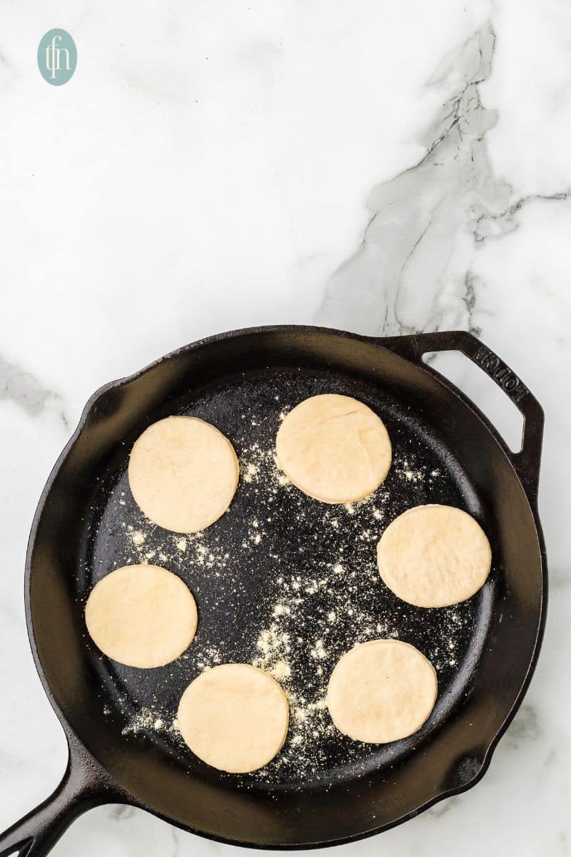 A skillet sprinkled with flour and has 6 circle doughs.