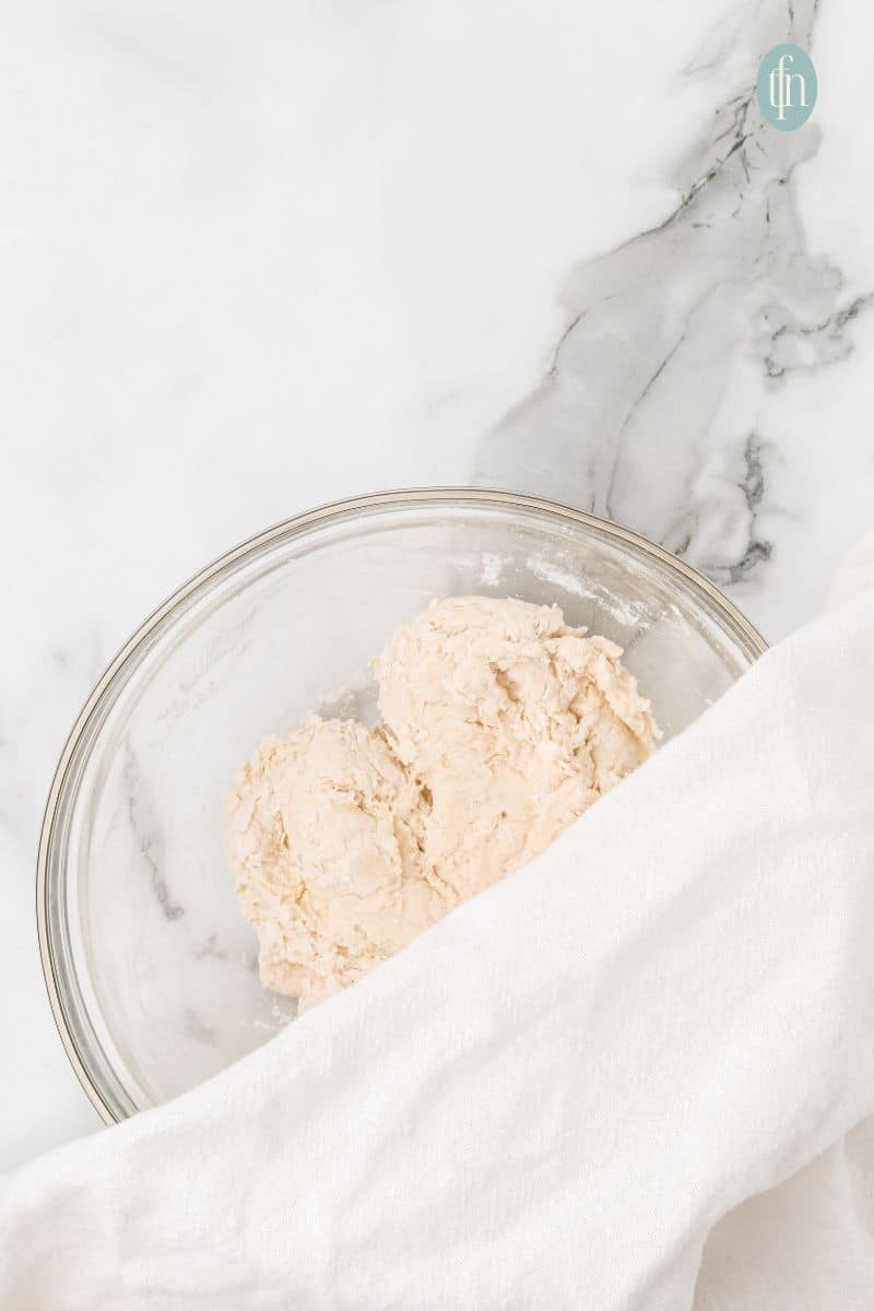 A bowl of dough, half covered with a towel.