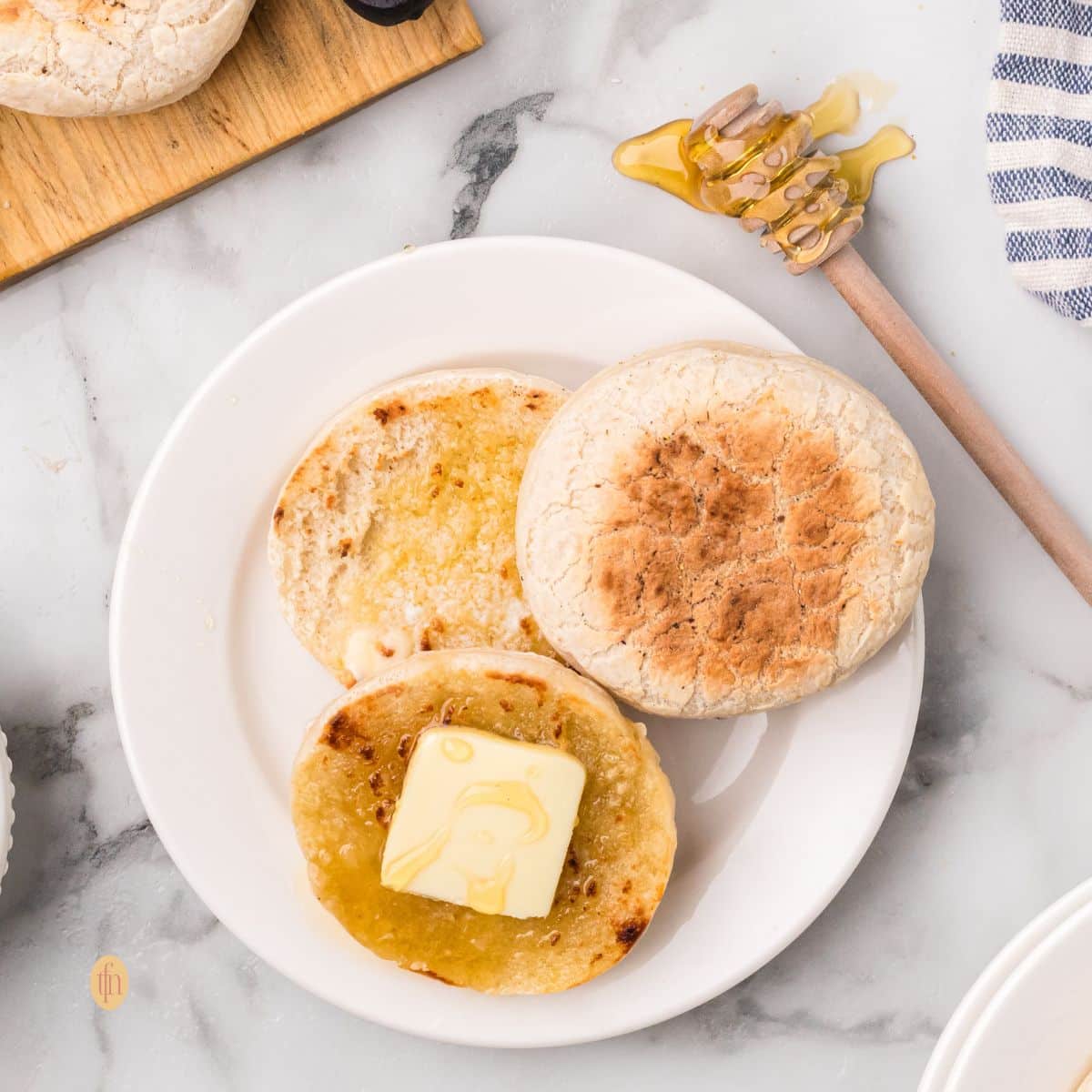 A plate of english muffin with butter on top.