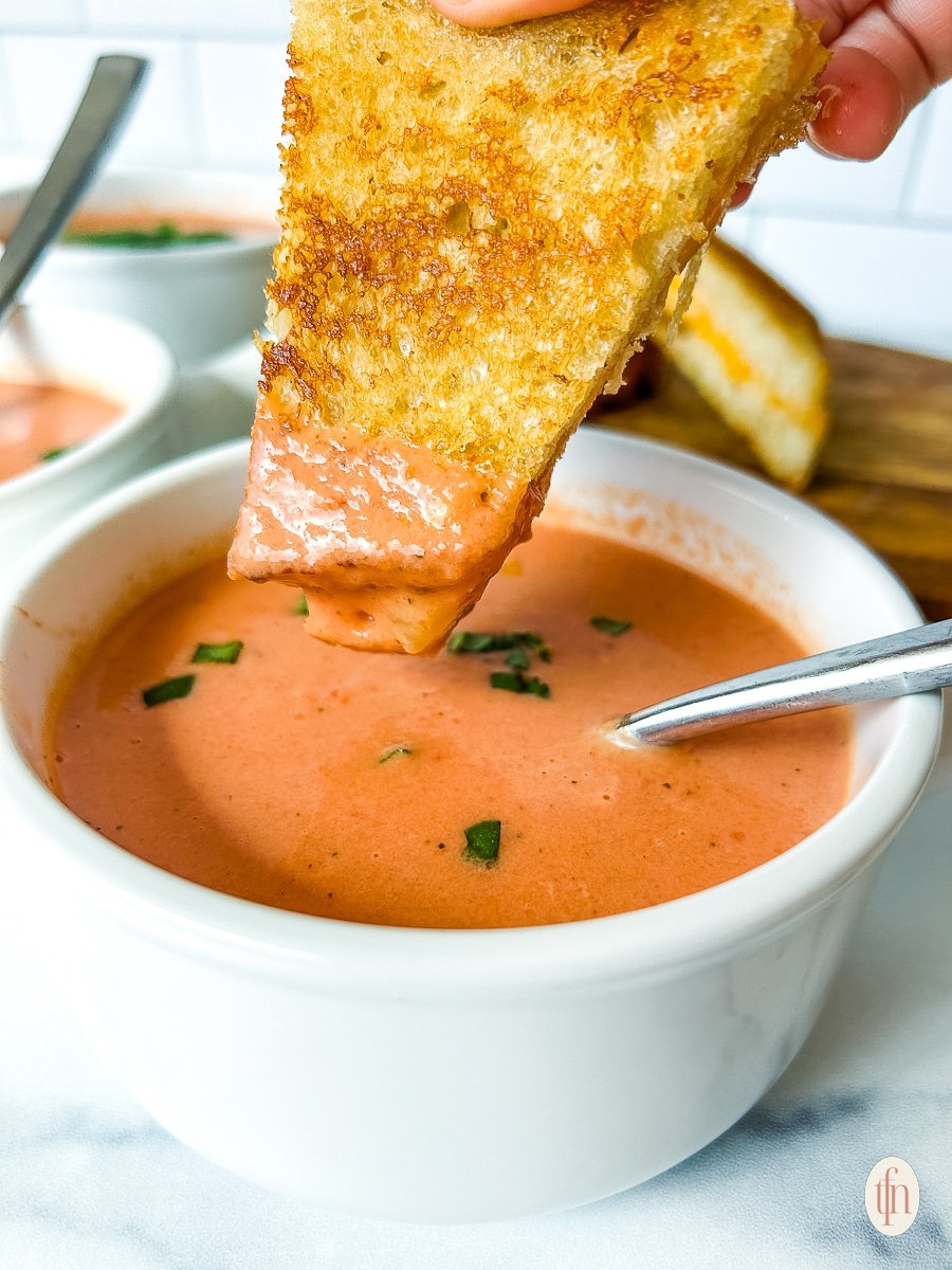 Grilled cheese sandwich dipped into a bowl of tomato soup.