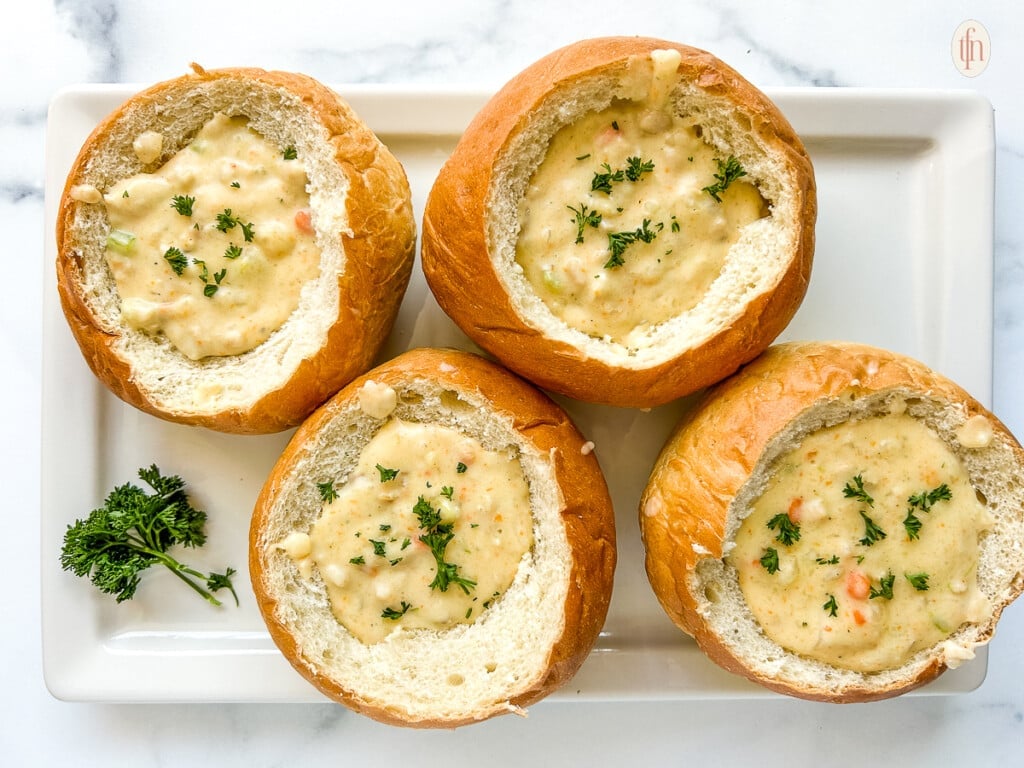 Four bread bowls filled with clam chowder on a white platter.