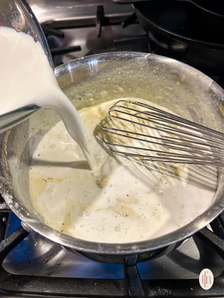 Pouring milk into soup mix on stove.