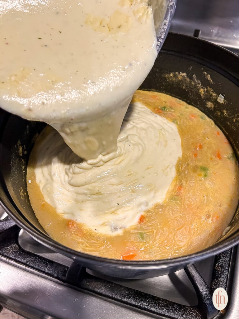 Pouring roux into soup mix on stove. 