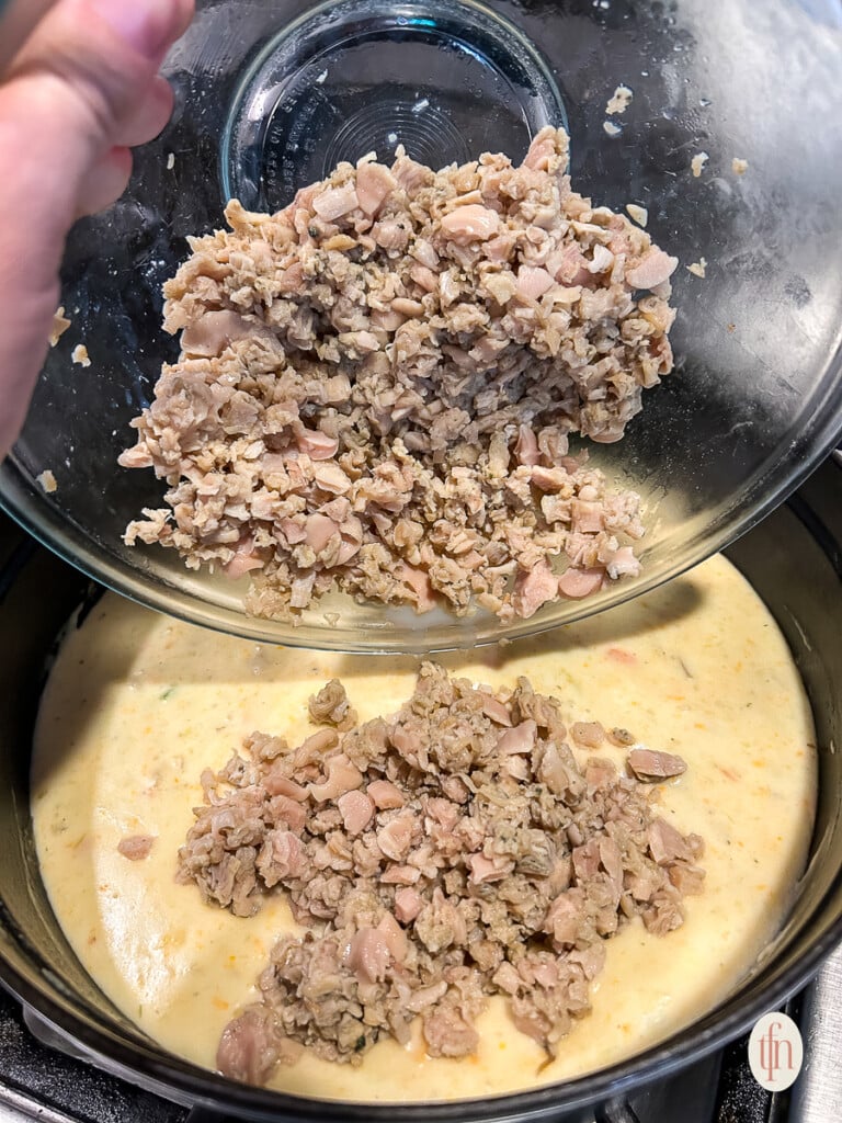 Pouring meat into soup mix on stove. 
