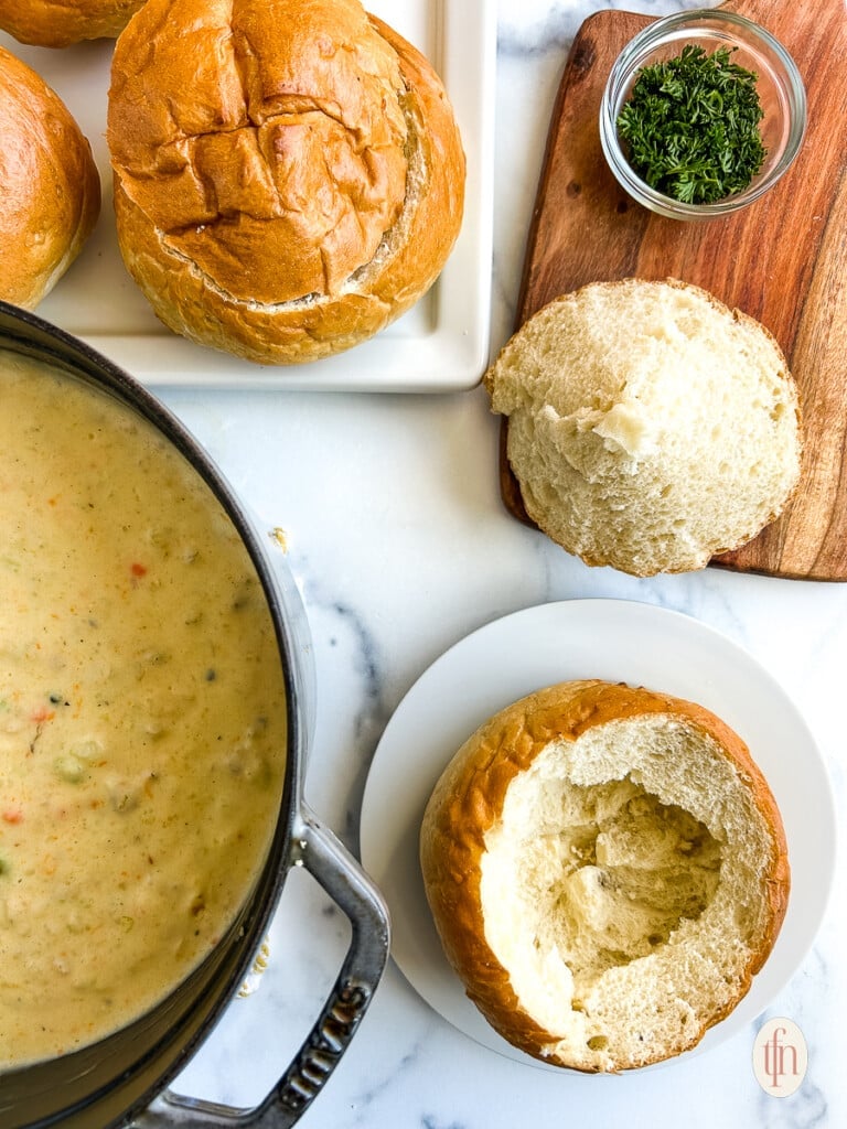 Empty bread bowl next to a pot of clam chowder. 