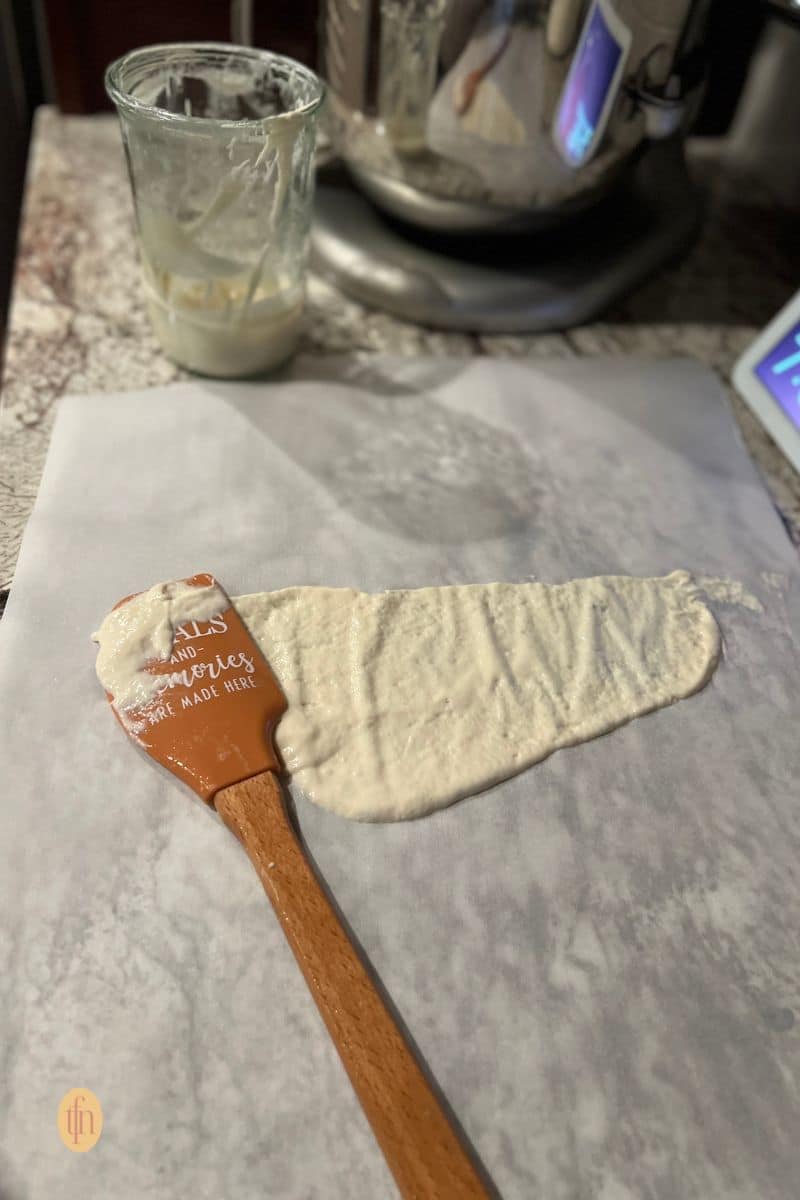Sourdough starter spread on a parchment paper with a rubber scrapper.