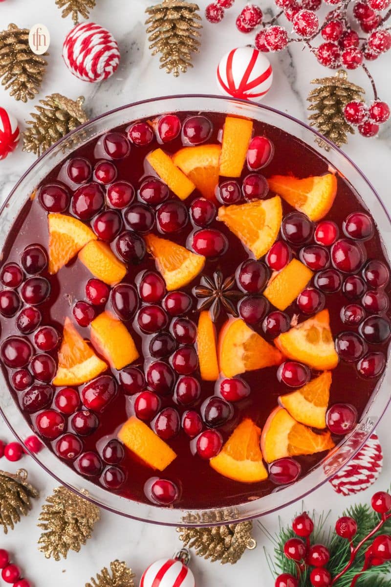 A beautiful non-alcoholic Christmas punch in a glass bowl, floating with bright red cranberries, orange slices, and a whole star of anise.