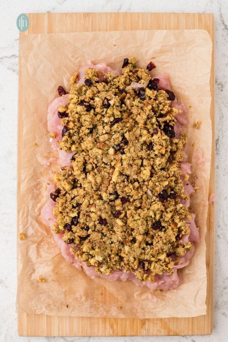 An overhead shot of the flattened raw turkey breast tenderloin spread with a thick layer of the cranberry and pecan stuffing mixture.