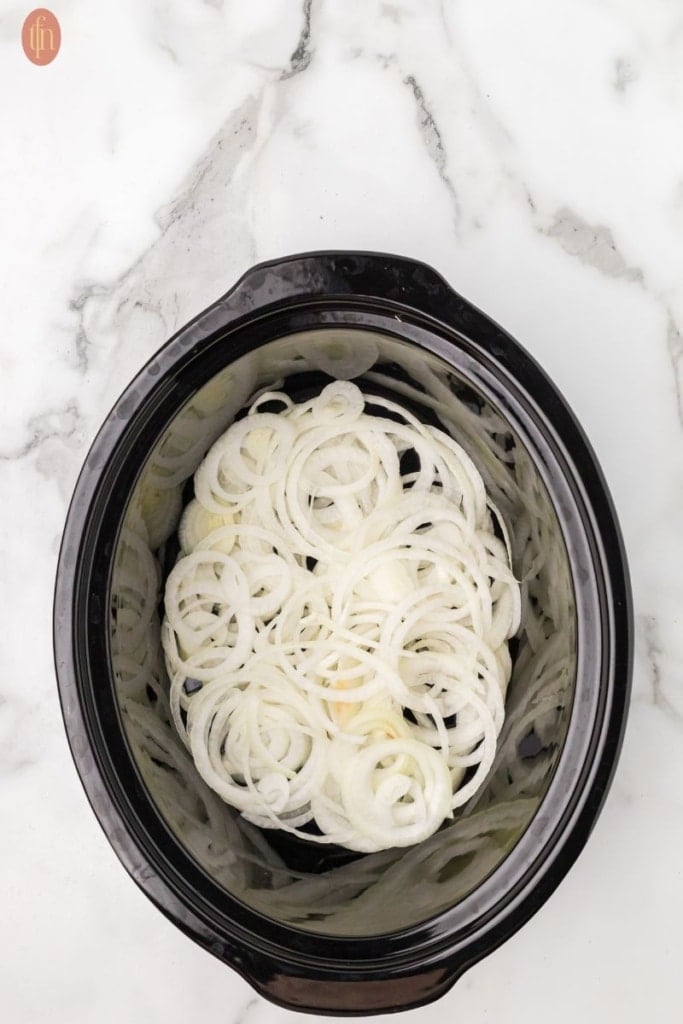 a prep image of sliced onions in crockpot for Slow Cooker Country Style Ribs.