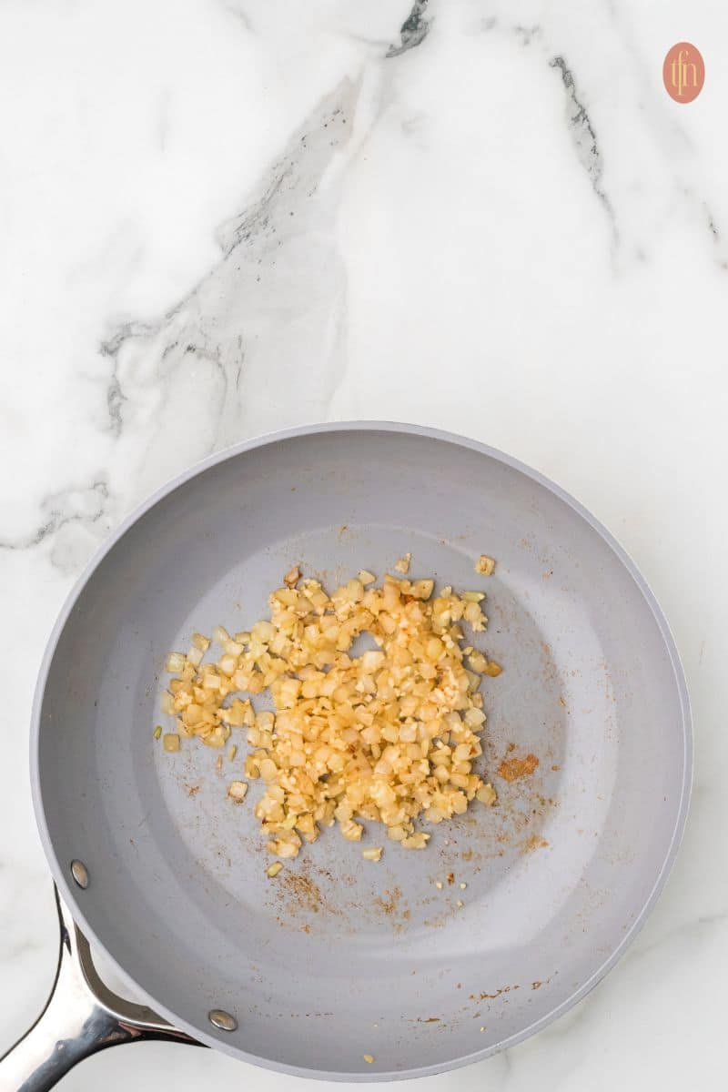 a skillet wit stirred onion, garlic and cumin.