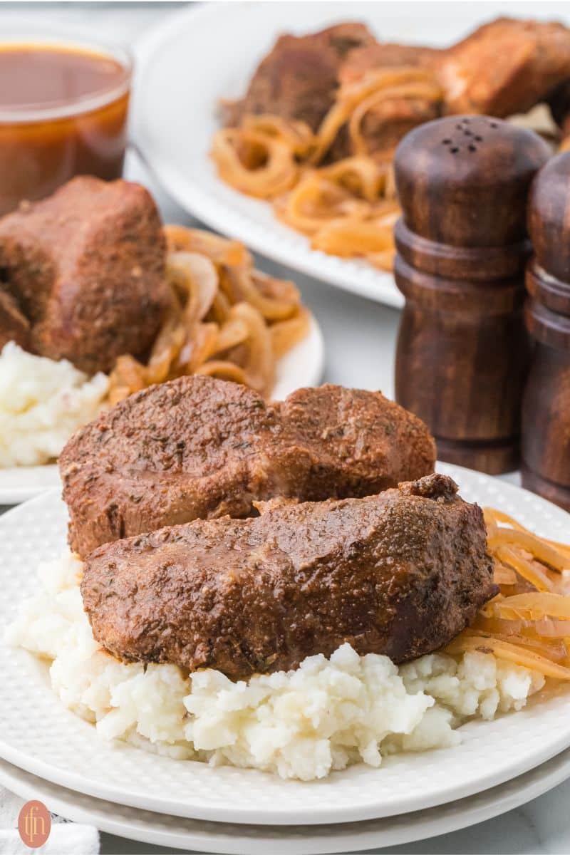 a plate of Slow Cooker Country Style Ribs on top of mashed potatoes with the platter of the remaining food in the background and salt and pepper shakers.