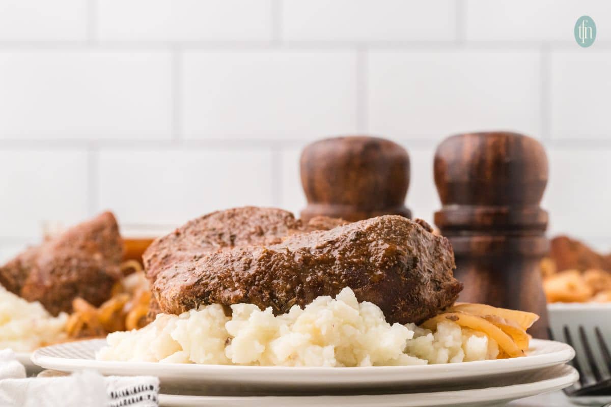 a country style rib plated with mashed potatoes and cooked onions with salt and pepper shakers in the background.