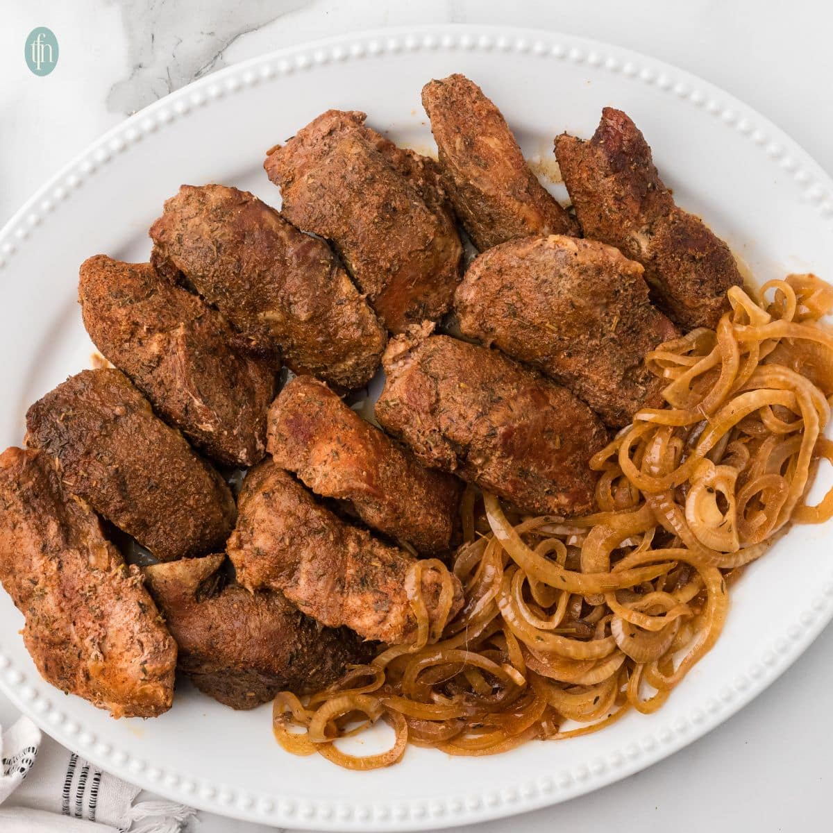 square photo of a platter of Boneless pork ribs and onions.