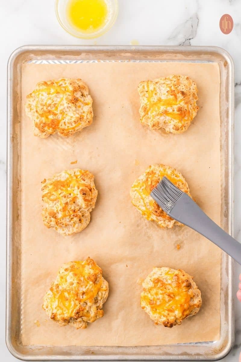 Cheddar biscuits on a baking sheet with parchment paper and pastry brush.