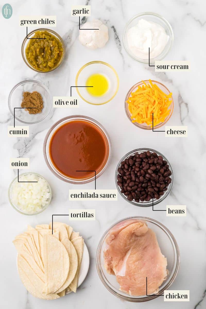chicken for enchiladas in crock pot ingredients: green chiles, garlic, sour cream, olive oil, cumin, cheese, onion, enchilada sauce, beans, tortillas, and chicken,
