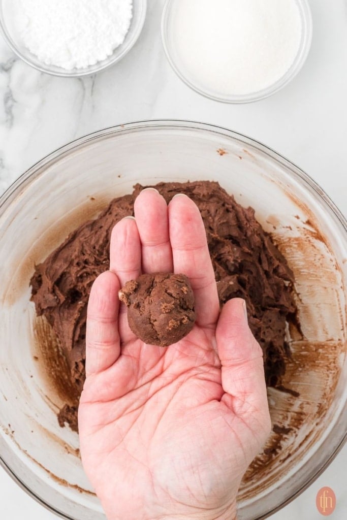 holding a roll dough balls with a bowl of dough mixture in the background.