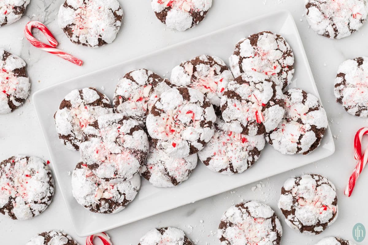 a plate of Christmas crinkle cookies with more cookies and candy cane on the side.