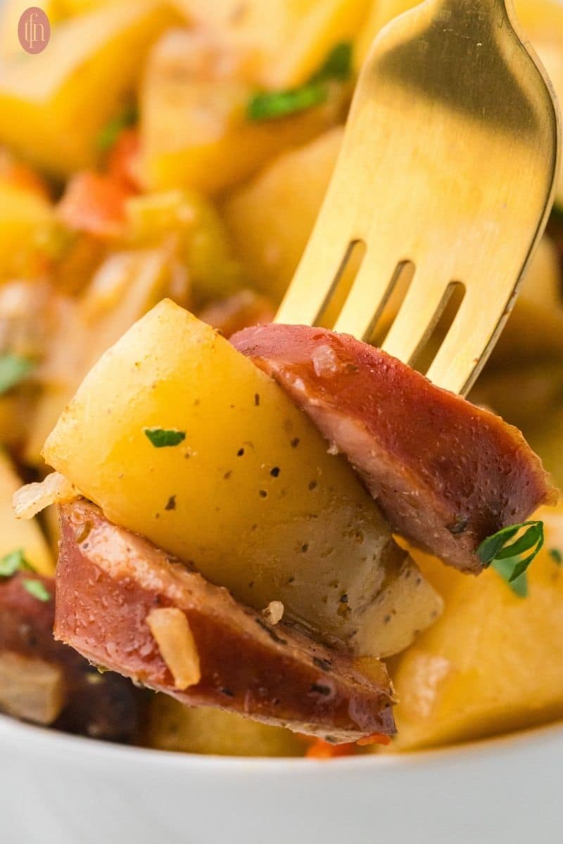 a fork stacked with crockpot sausage & potatoes sprinkled with parsley.