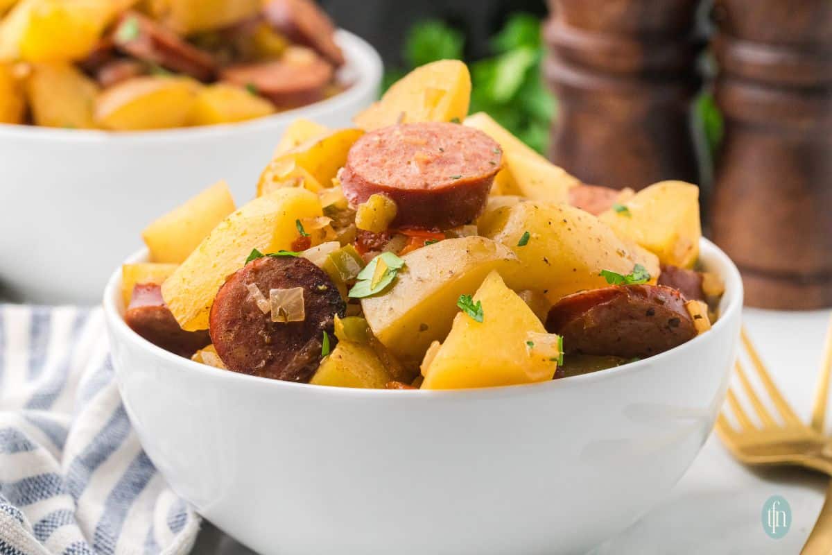 a horizontal image of a bowl of sausages and potatoes in slow cooker