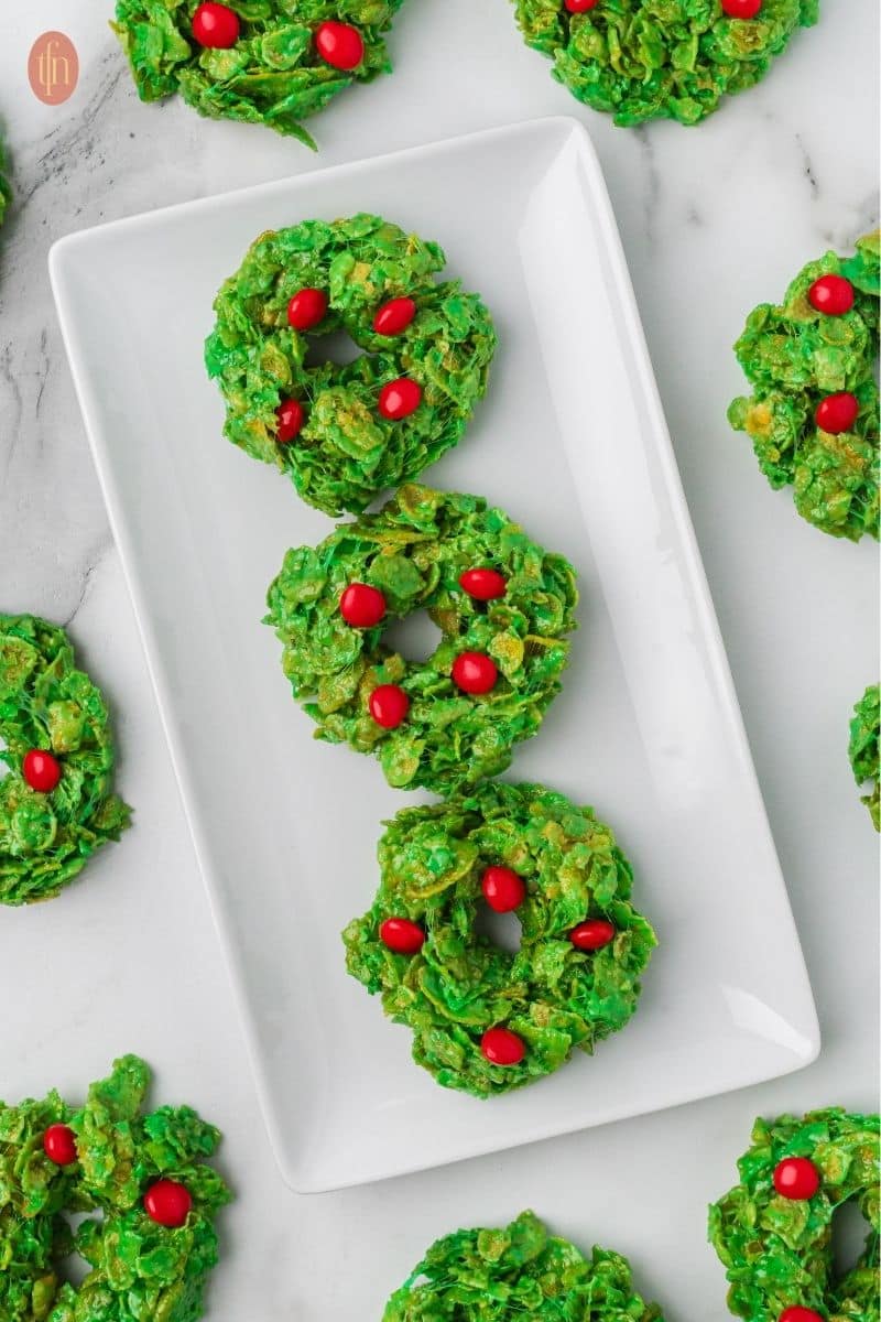 a plate of no bake Christmas cookies made with cornflakes and with red cinnamon candies on top.