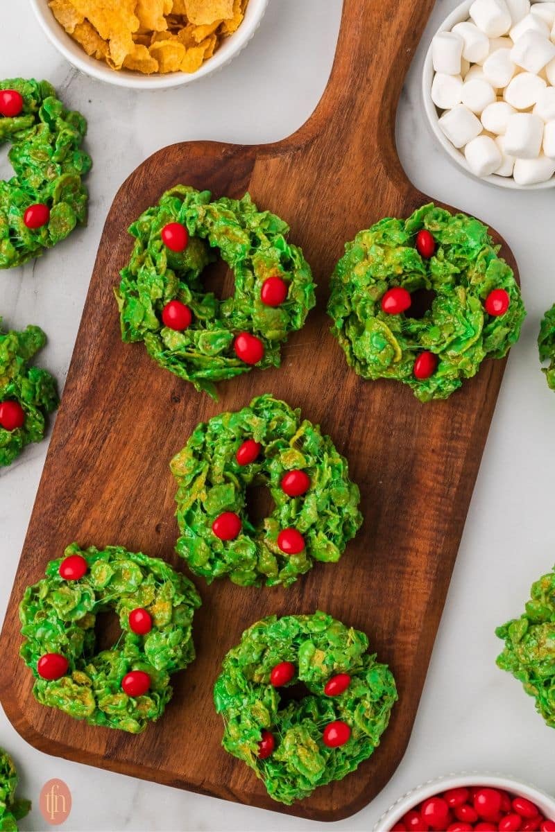 a photo of no bake cookies with cornflakes with a bowl of cornflakes cereal, mini marshmallows and red cinnamon candies on the side.