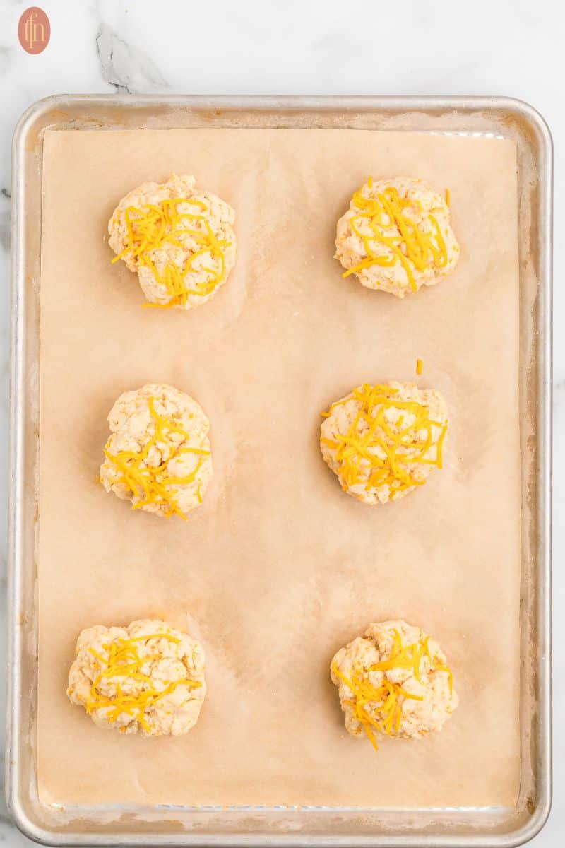 Cheddar biscuit batter ball on a baking sheet with parchment paper.