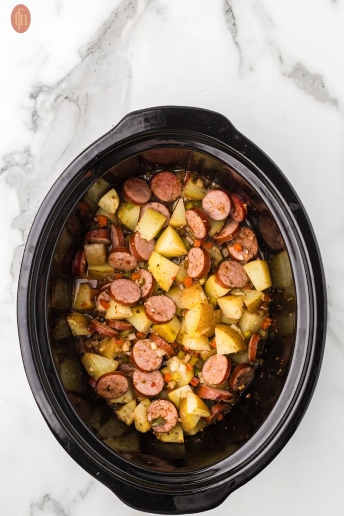 a full crockpot with ingredients for sausages and potatoes in slow cooker.