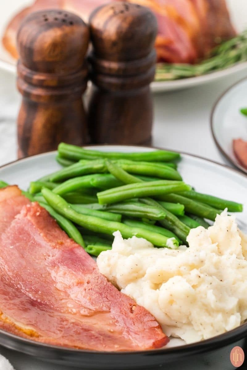 a plate of a cola ham with mashed potatoes and green beans.
