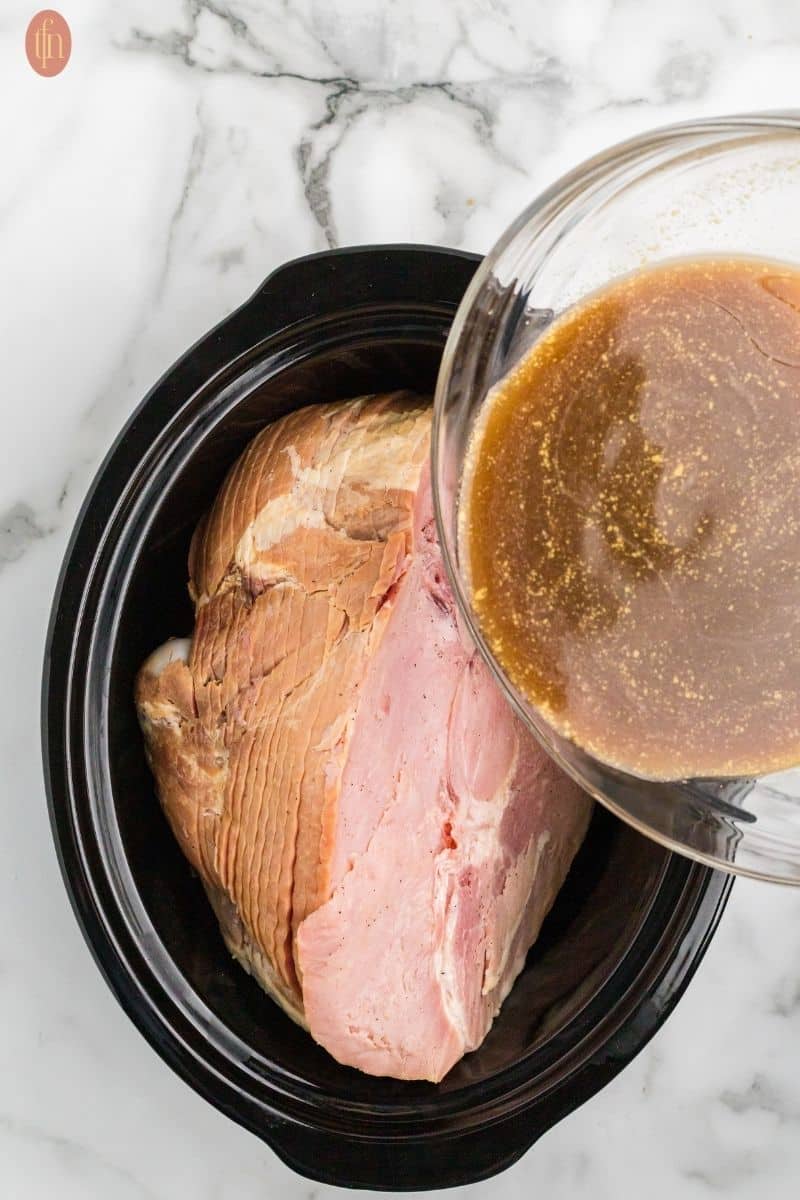 a ham in the microwave safe bowl poured with stirred sugar, cola, mustard, and pineapple juice.