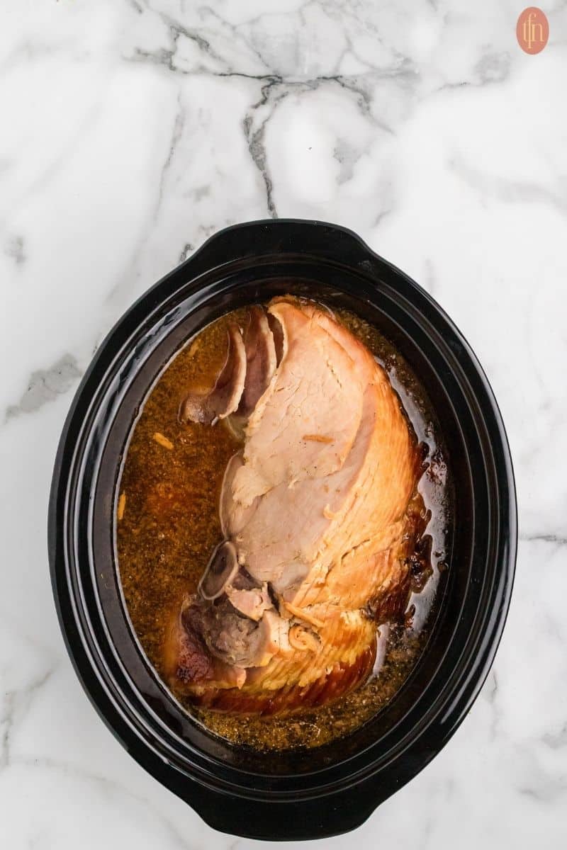 a ham with stirred sugar, cola, mustard, and pineapple juice in a small, microwave safe bowl.