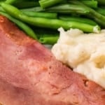 a plate of a dr pepper ham with mashed potatoes and green beans.