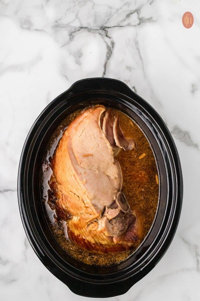 a ham with stirred sugar, cola, mustard, and pineapple juice in a small, microwave safe bowl.