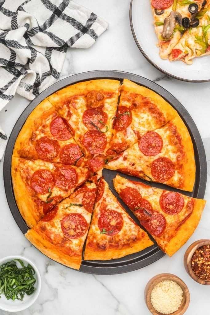 a homemade pizza served in a round pan with three small bowls of seasonings on the side.