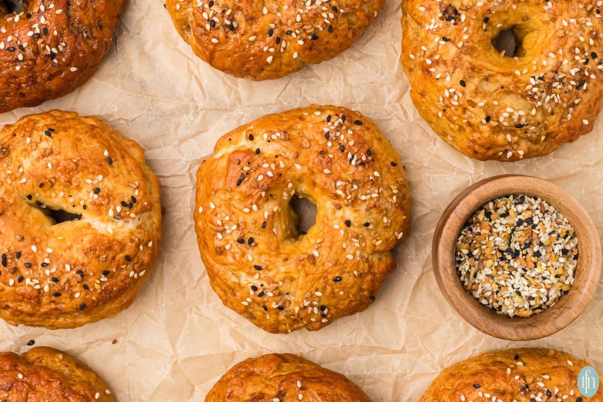 an image of sourdough bagels on parchment paper with a small bowl of everything but the bagel seasoning.
