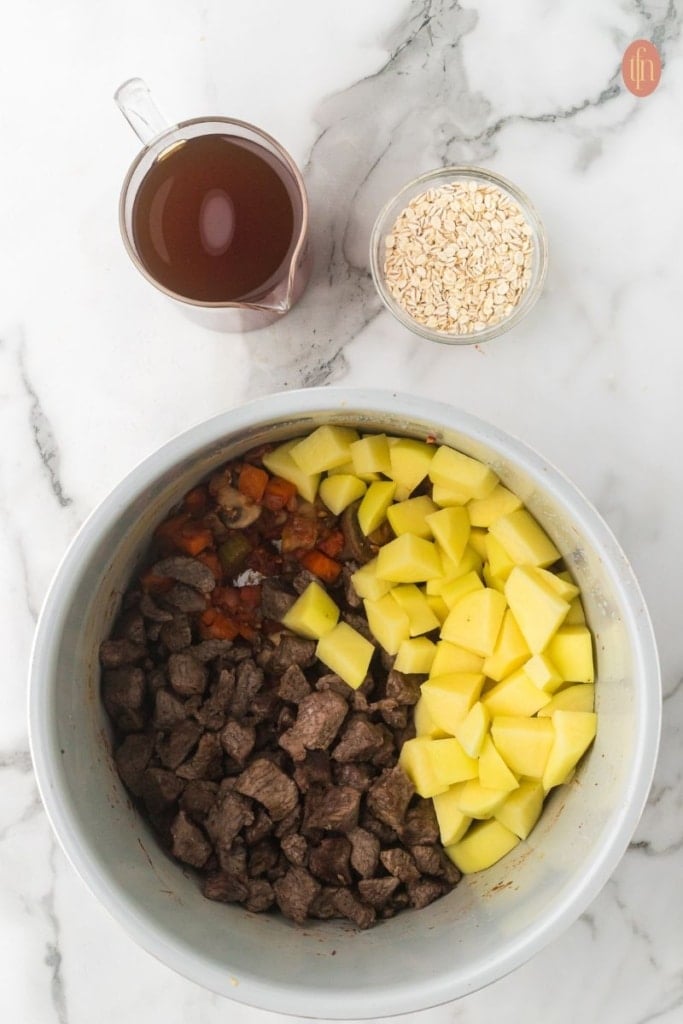 a pot of saut&eacute;ed vegetables with beef and potatoes at the top.