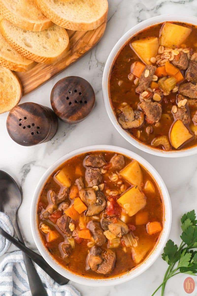 two bowls of Instant Pot beef and barley soup with bread on the side.
