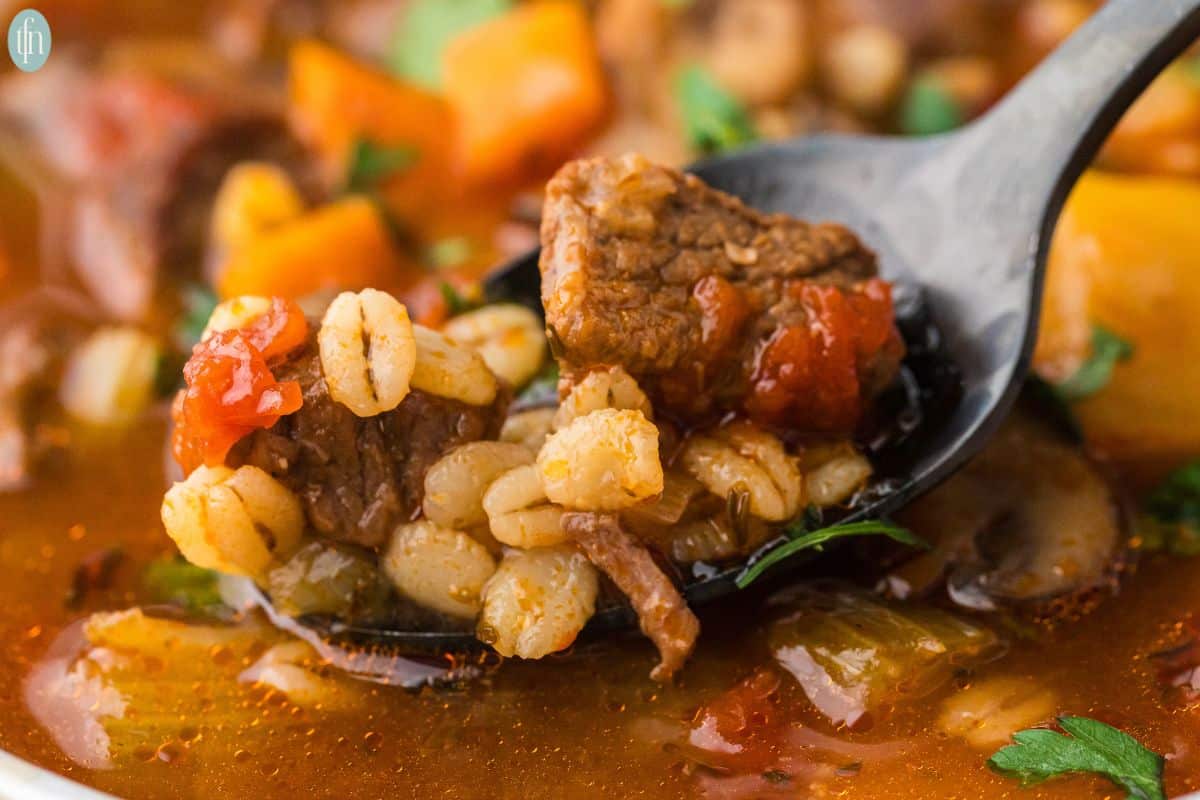 a close up shot of instant pot beef and barley soup in a spoon.