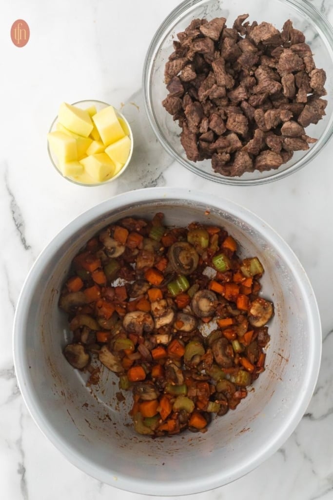 a pot of saut&eacute;ed vegetables with a bowl of potatoes and a bowl of browned beef.