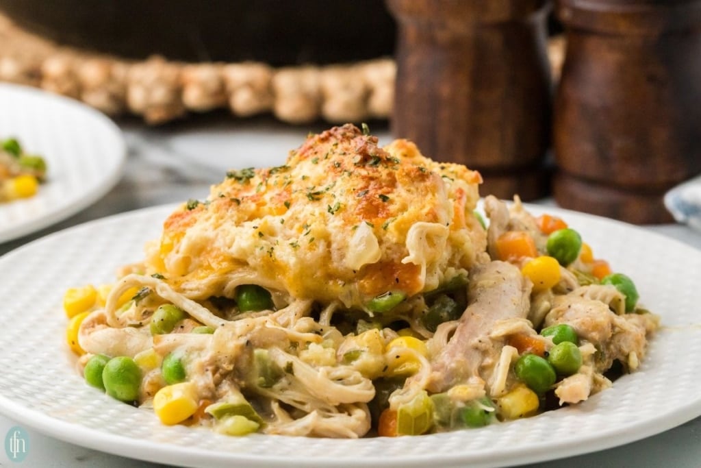 a close up shot of chicken pot pie with biscuit on a plate.