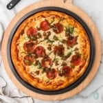 pizza topped with pepperonis and cheese served on a black circular pan placed on a wooden board.