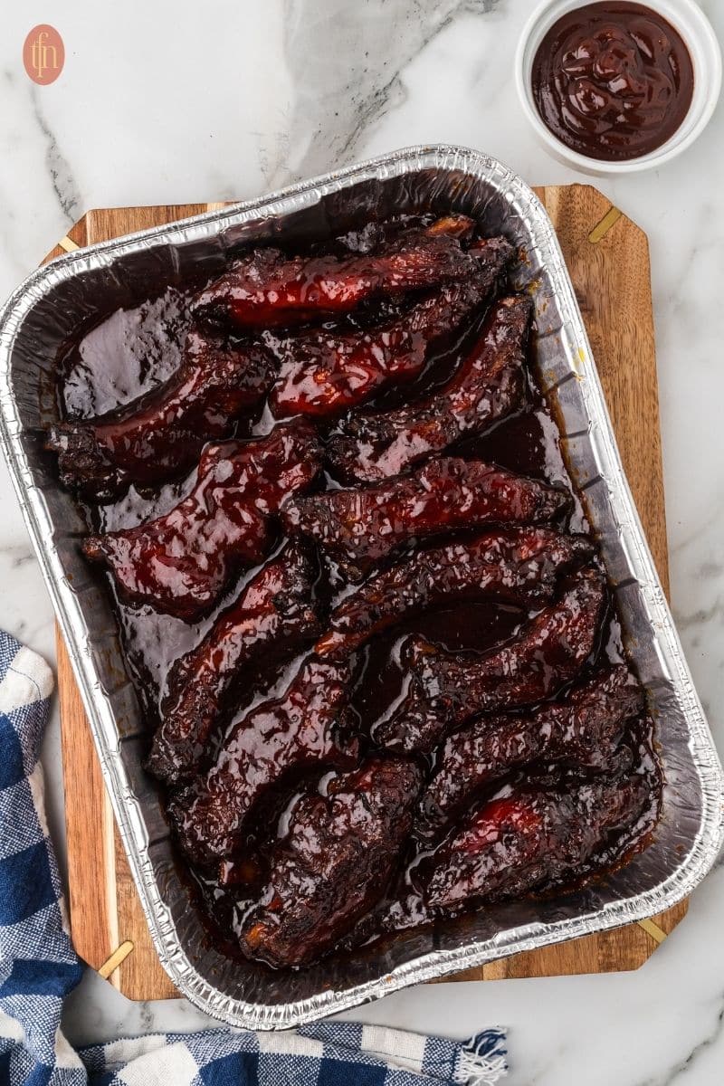 smoked party ribs in a rectangular aluminum foil pan.
