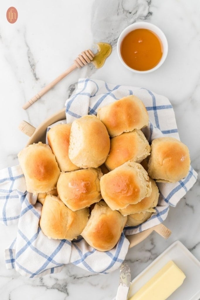 an image of a golden brown dinner rolls in a wooden bowl and blue checkered cloth.